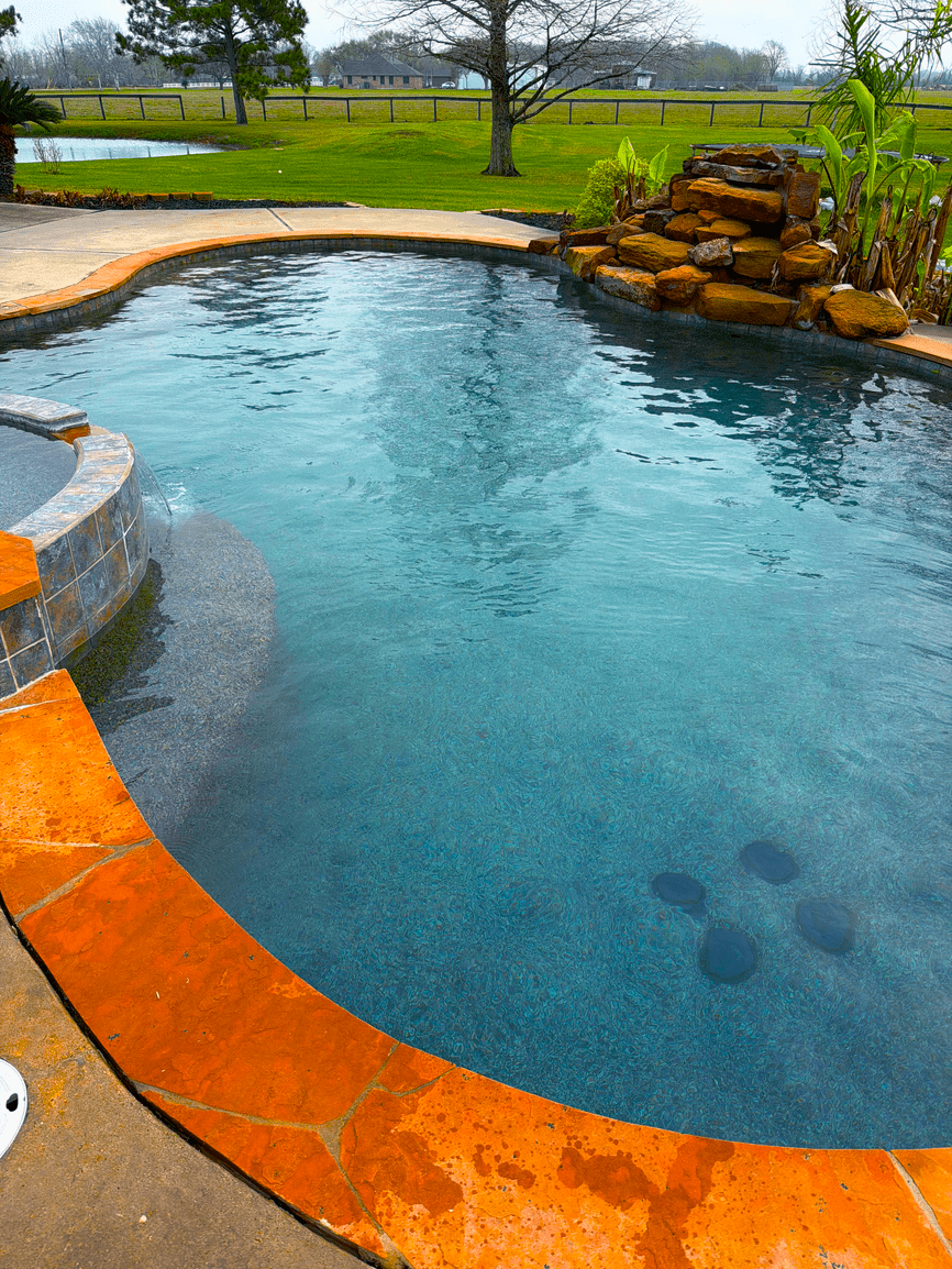Blue backyard pool with a rock waterfall, from Penny’s Pool Service’s gallery